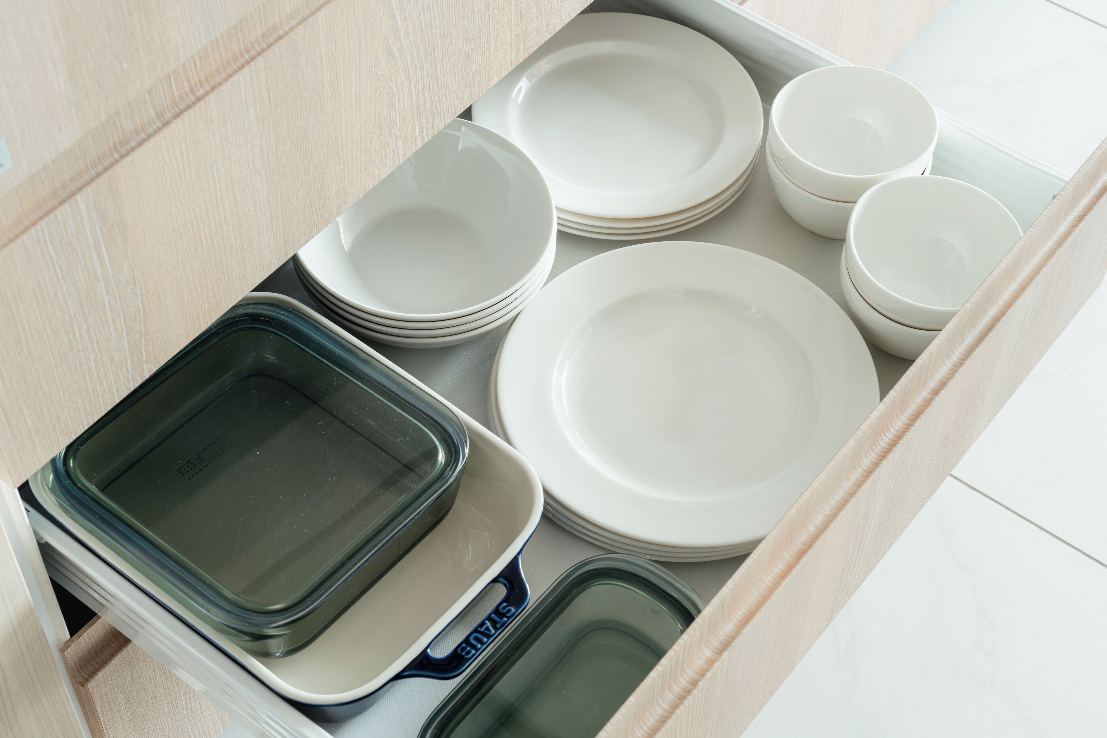 A drawer containing various kitchenware items including plates, bowls, and a glass baking dish.