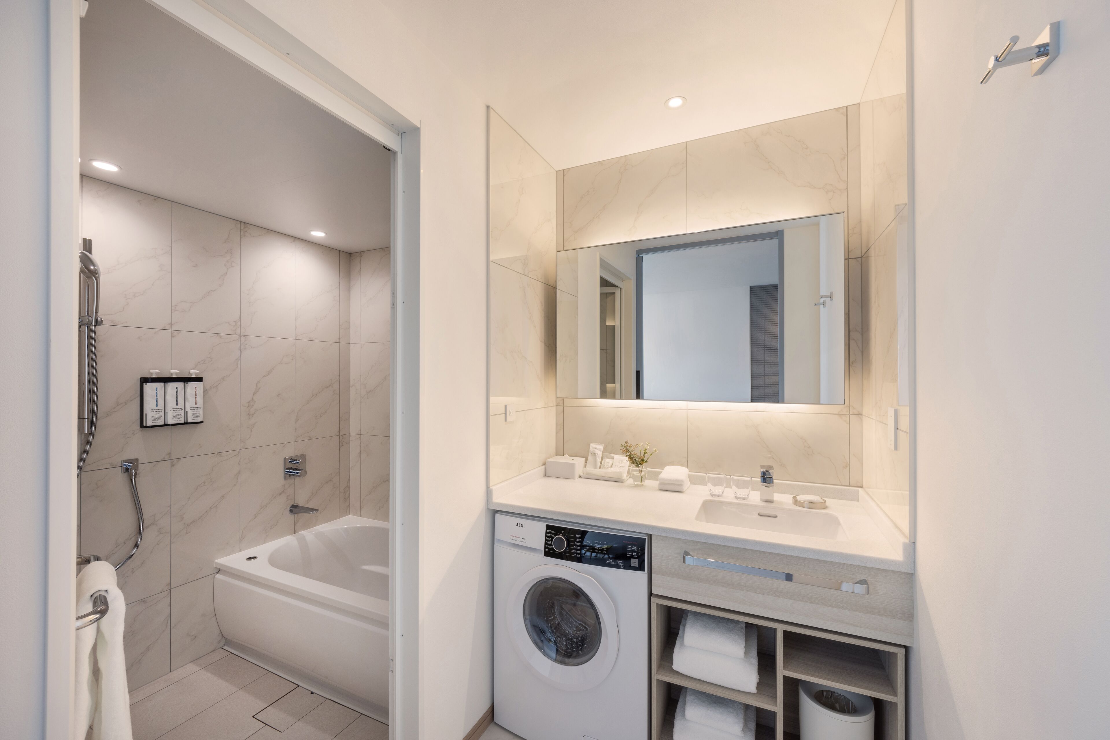 A modern bathroom with a built-in washing machine, a bathtub, and a large mirror above the sink.