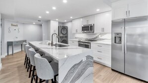 A modern kitchen with white cabinetry, stainless steel appliances, and a marble island with bar stools.