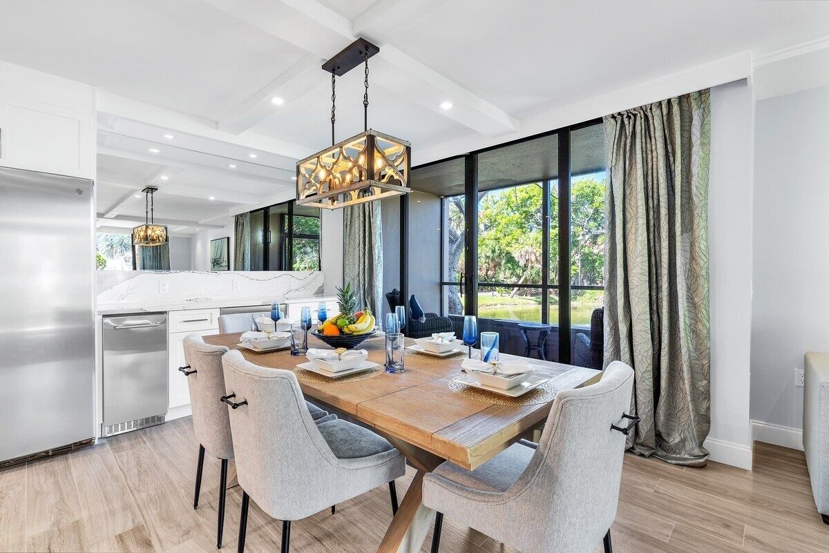 A modern kitchen with a wooden dining table, grey chairs, and a hanging light fixture.