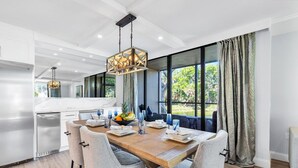 A modern kitchen with a wooden dining table, grey chairs, and a hanging light fixture.