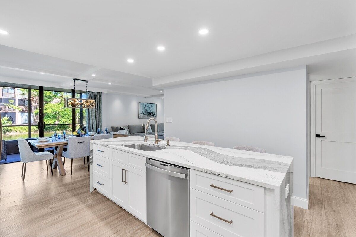 A modern kitchen with white cabinetry, a large island with a sink, and a dining area with a table and chairs.