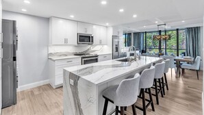 A modern kitchen with white cabinetry, a marble island, and bar stools.