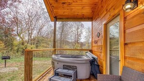A wooden deck with a hot tub, a wicker sofa, and a covered area with a lantern. - Couple's Retreat: HotTub-FirePit-Grill-Pets-Wifi (Sevierville)