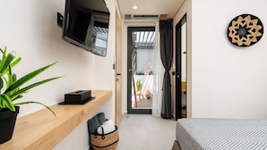 Un dormitorio moderno con una cama, un televisor montado en la pared, un estante de madera con una planta, una cesta y una pieza decorativa en la pared.