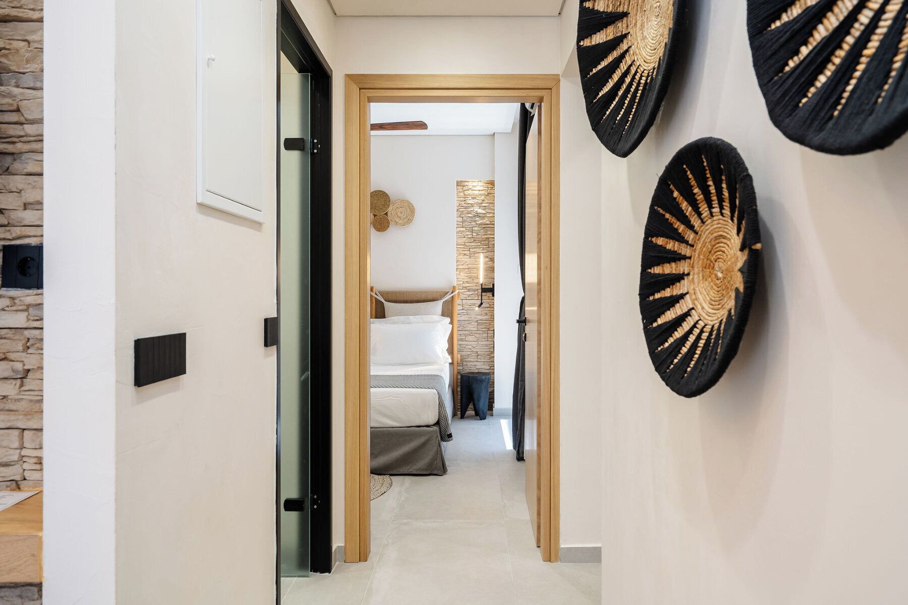 Een gang met een stenen muur aan de linkerkant, een bed met een stenen muur als achtergrond, en een houten deurkozijn.