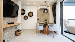 Una sala moderna con una televisión de pantalla plana, pared de piedra, platos decorativos, una mesa de comedor con sillas y un ventanal corredizo a un balcón.