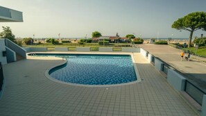 Une piscine au design incurvé, entourée d’une terrasse carrelée et offrant une vue sur la plage et l’océan.