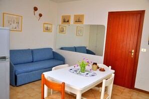 Un espace de vie compact avec un canapé bleu, une petite table à manger agrémentée d’un vase de fleurs et une porte rouge.