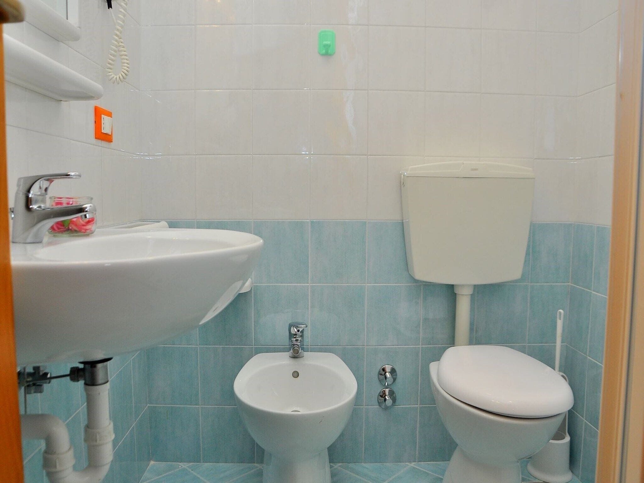 A bathroom with a sink, bidet, toilet, and a visible pipe.