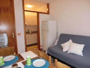 A compact living space with a kitchenette, a sofa, and a dining table set for two.