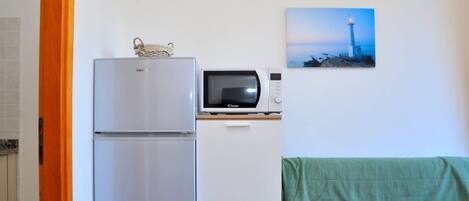 A compact kitchenette with a refrigerator, microwave, and a small cabinet. A painting of a lighthouse is on the wall.