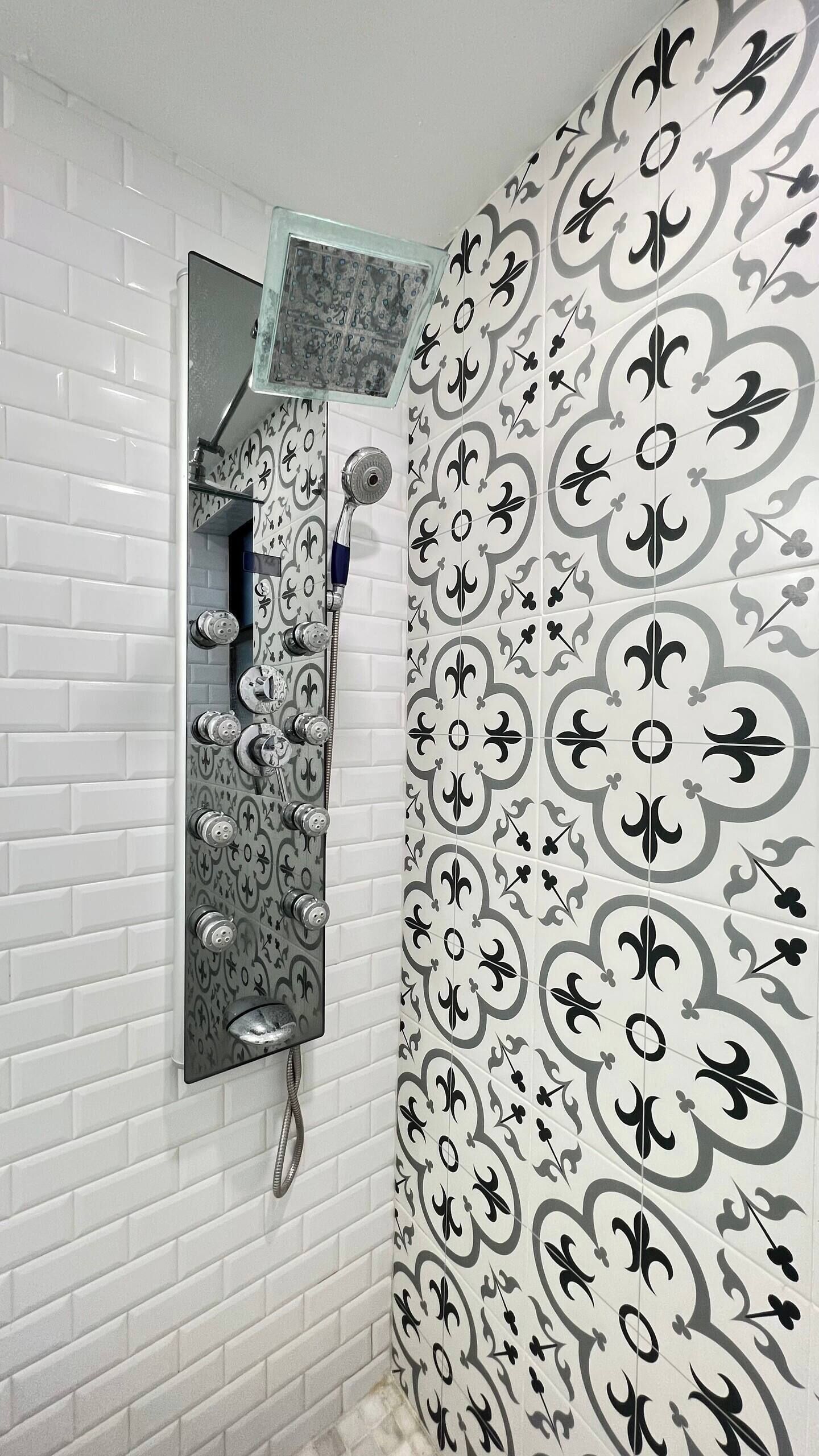 A bathroom with white subway tiles, a shower with a glass enclosure, and decorative black and white tiles on the walls.