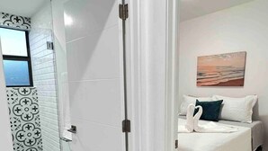 Quarto de hotel com cama, um quadro e área de chuveiro com azulejos estampados.