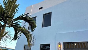 Um edifício moderno de dois andares, com fachada branca, um portão preto e uma pequena área de jardim com uma palmeira.