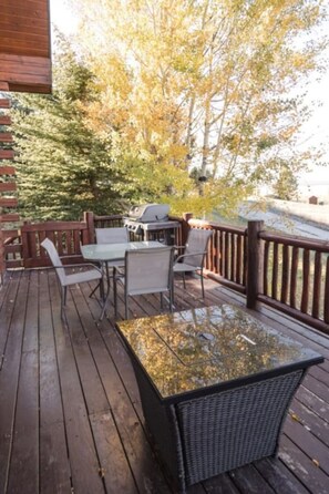Eine Holzterrasse mit Gartenmöbeln, darunter ein Tisch, Stühle und ein Grill.
