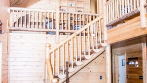 Ein Holzinnenraum mit einer Treppe, die zu einer oberen Ebene führt, einer Essecke mit Tisch und Stühlen sowie einem Deckenventilator.