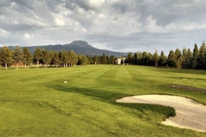 Ein Golfplatz mit blauem Himmel, einem Berg im Hintergrund und einem gepflegten Rasen.