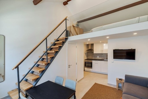 Eine moderne Wohnung mit einer Treppe zu einem Schlafzimmer-Loft, einer Küche mit integrierten Geräten und einem Wohnbereich mit Sofa und Fernseher.