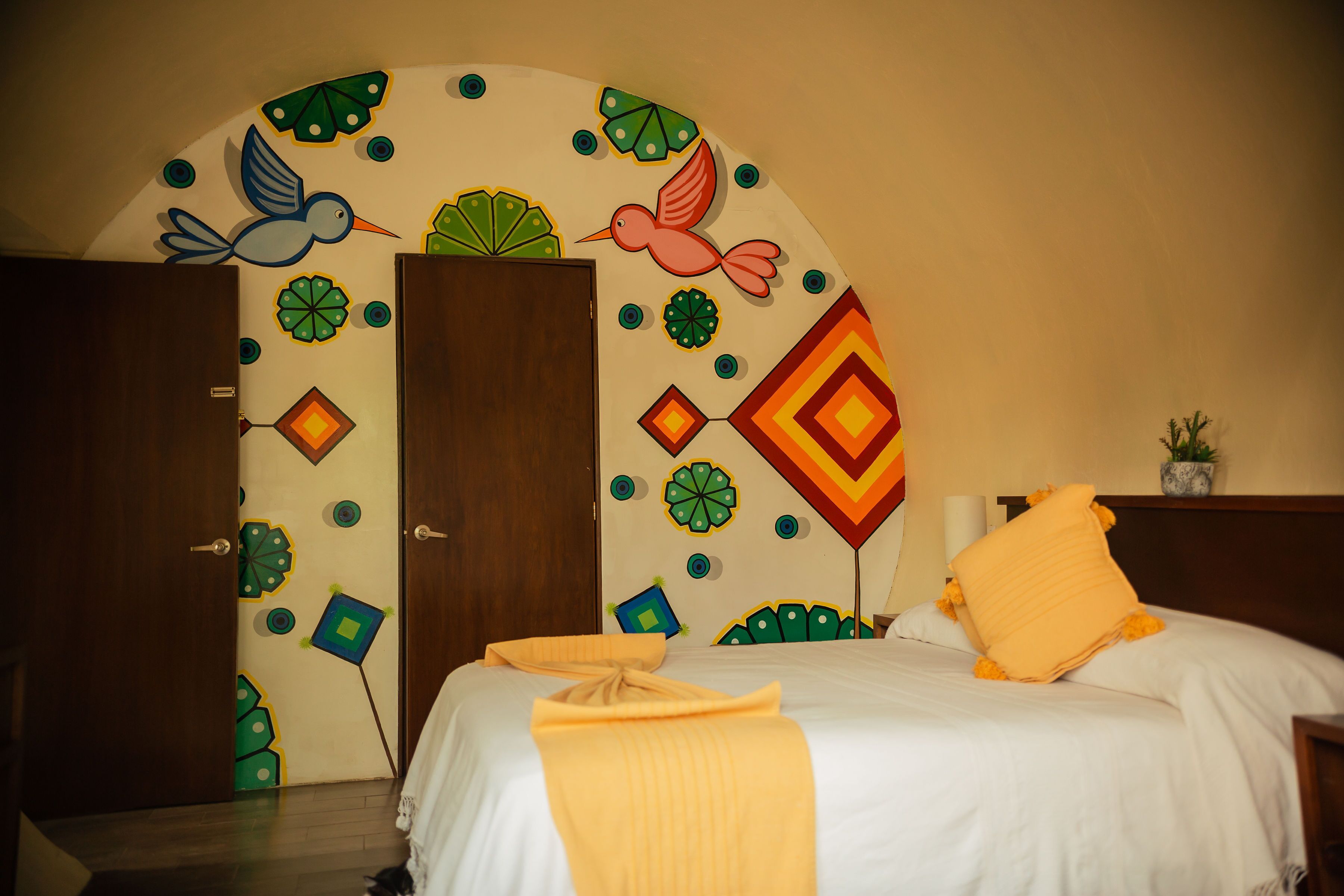 A hotel room with a bed, a door, and a wall with colorful geometric patterns.