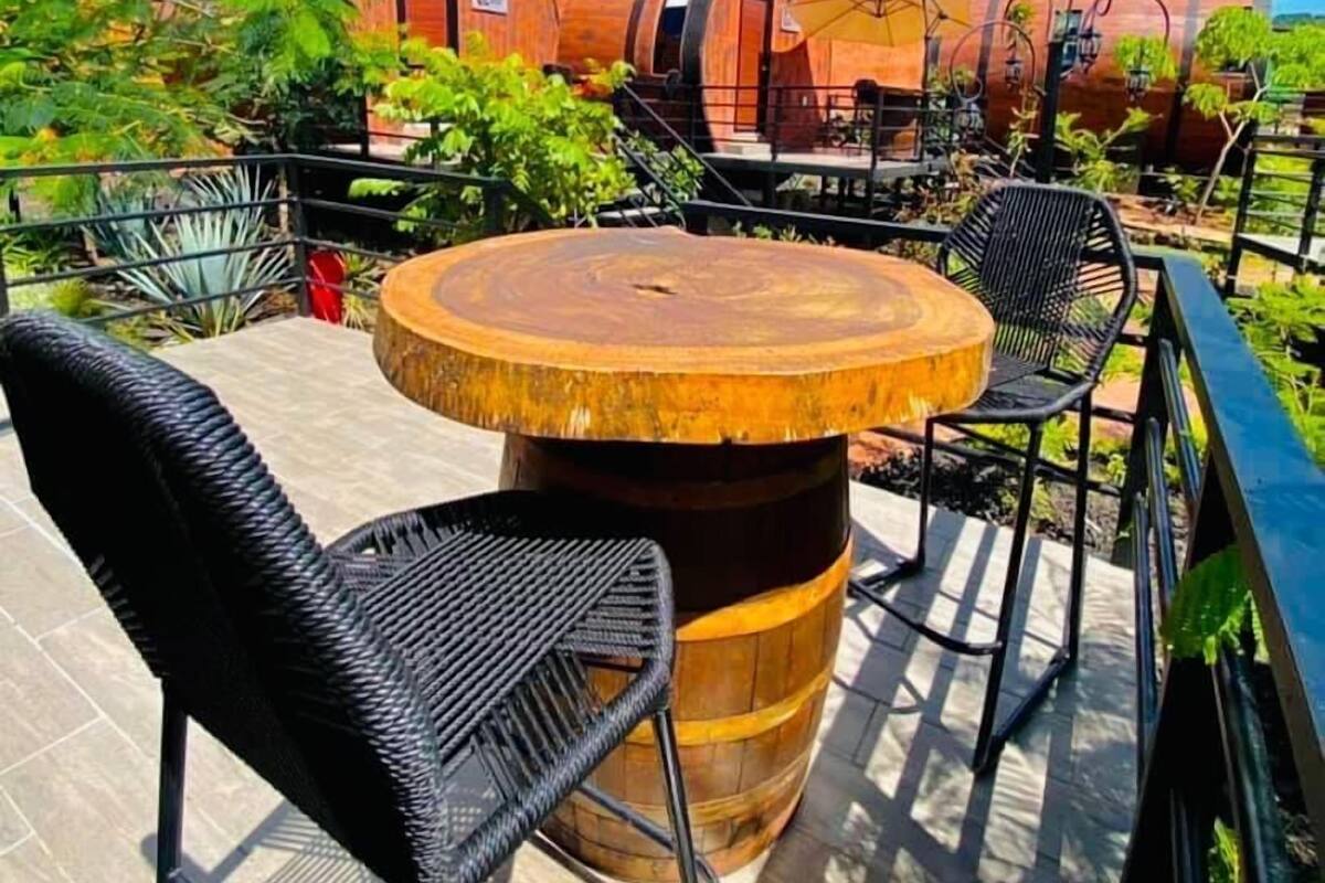 Une table ronde en bois, entourée de chaises, est placée sur une terrasse d’où l’on peut admirer, au loin, des bâtiments de forme cylindrique aux couleurs vives.