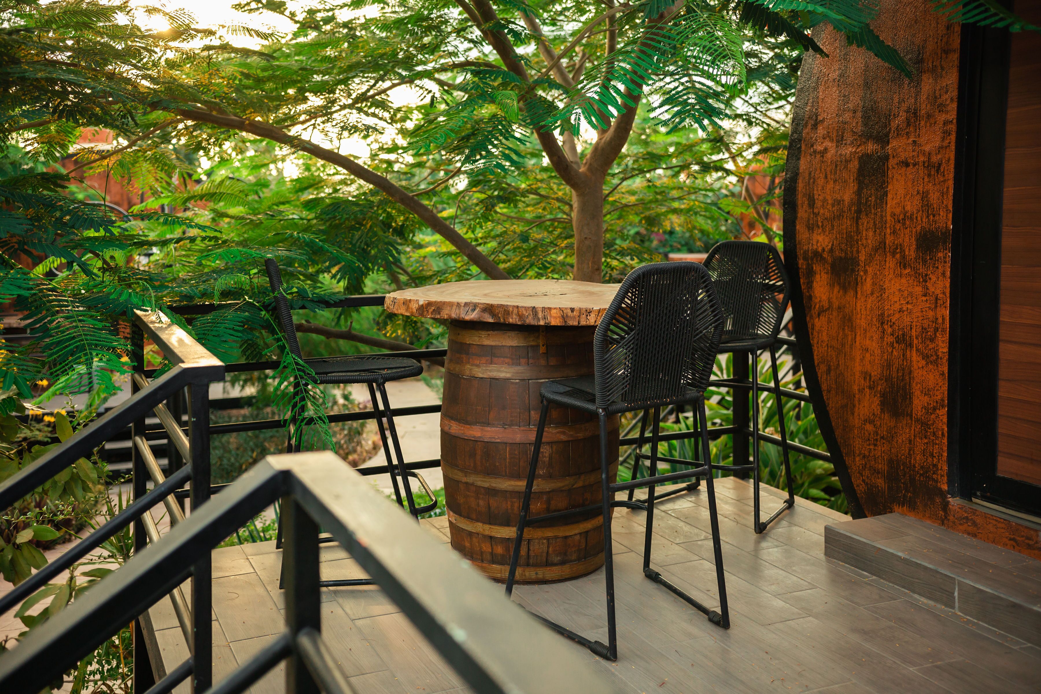 A wooden table with chairs, a metal railing, and a tree in the background.