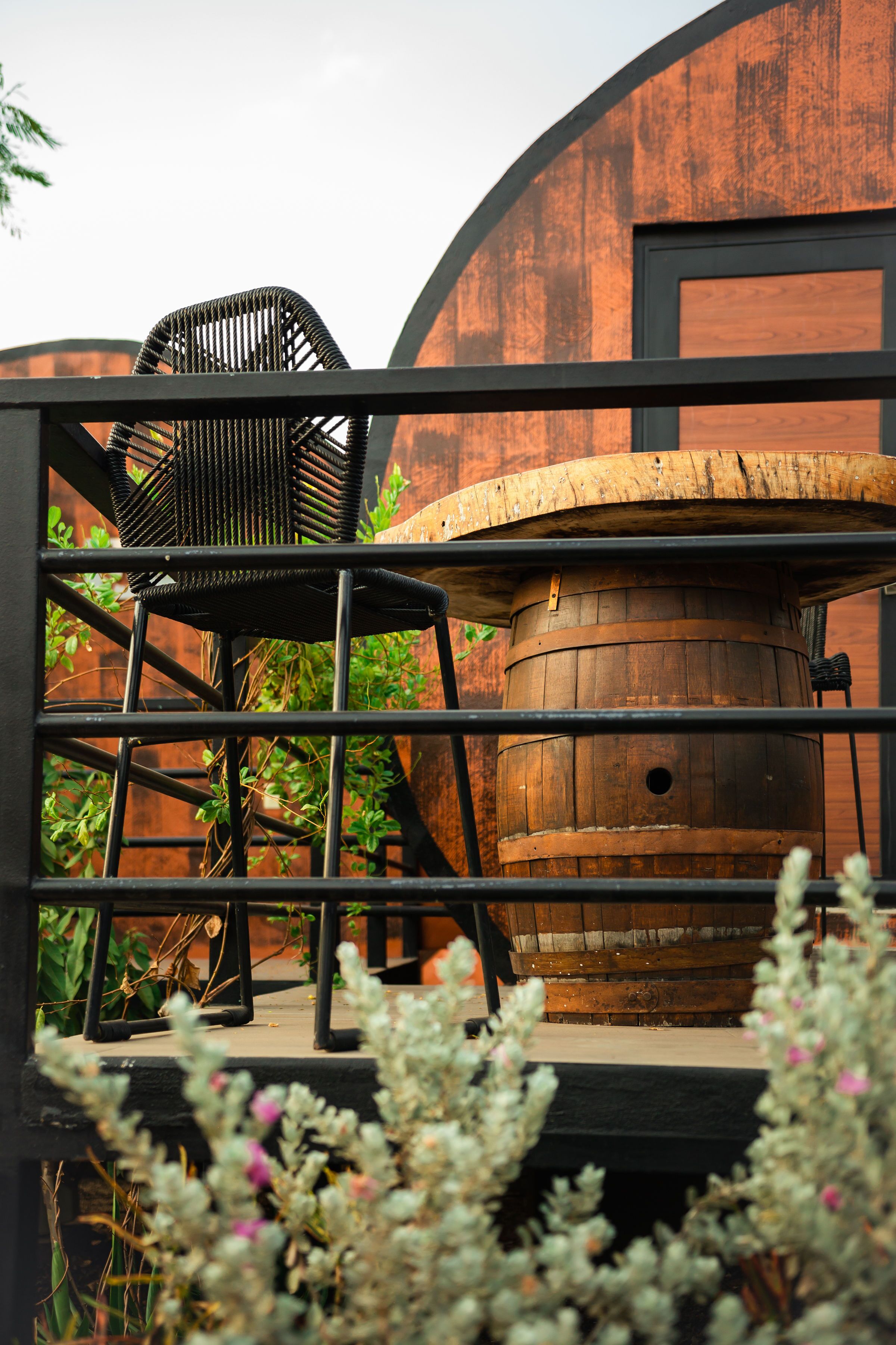 A rustic outdoor seating area with a wooden barrel and a metal chair.