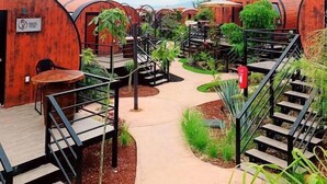Una serie de estructuras cilíndricas de madera con barandillas y escaleras de metal, rodeadas de follaje y un cielo despejado.