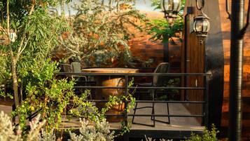 An outdoor seating area with a wooden table and chairs, surrounded by greenery and a brick wall.