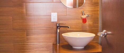 Un baño moderno con pared de madera, un lavabo blanco, un espejo grande y un inodoro.