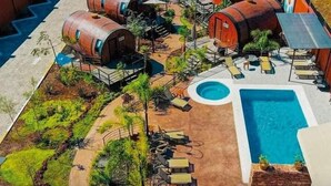 Un área de piscina con jacuzzi, sillones reclinables y estructuras de estilo rústico tipo barril.