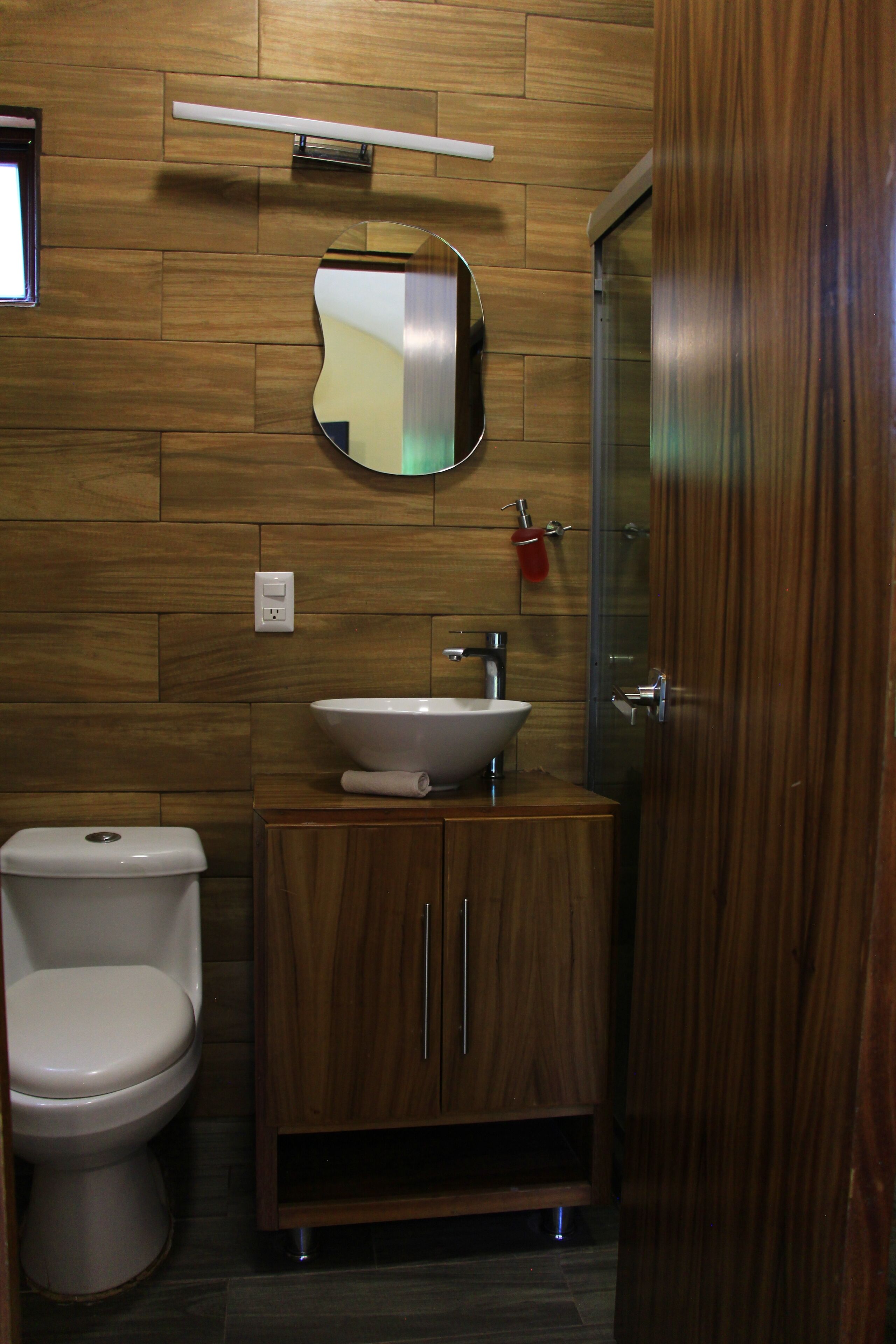 A bathroom with a wooden wall, a white sink, a mirror, and a toilet.
