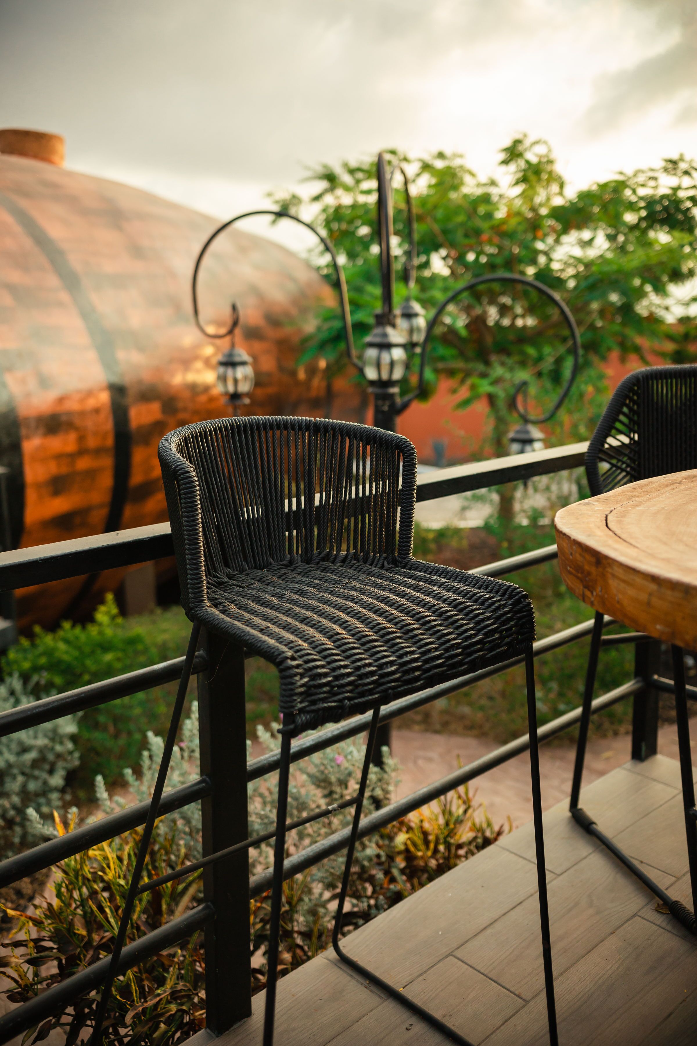 Una silla de mimbre y una mesa de madera en un patio exterior con barandilla de metal.