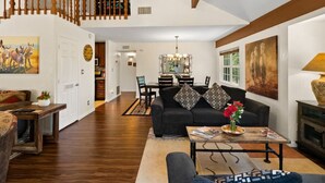 Un salon spacieux avec un canapé noir, une table à manger en bois et un escalier menant à l’étage supérieur.