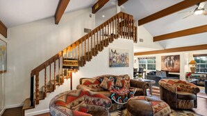 Un salon spacieux avec un escalier en bois, des meubles en cuir et de grandes fenêtres qui laissent entrer la lumière naturelle.