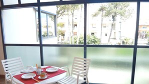 Ein Essbereich mit einem Tisch für zwei Personen, Stühlen und Blick auf ein Gebäude und Bäume durch große Fenster.