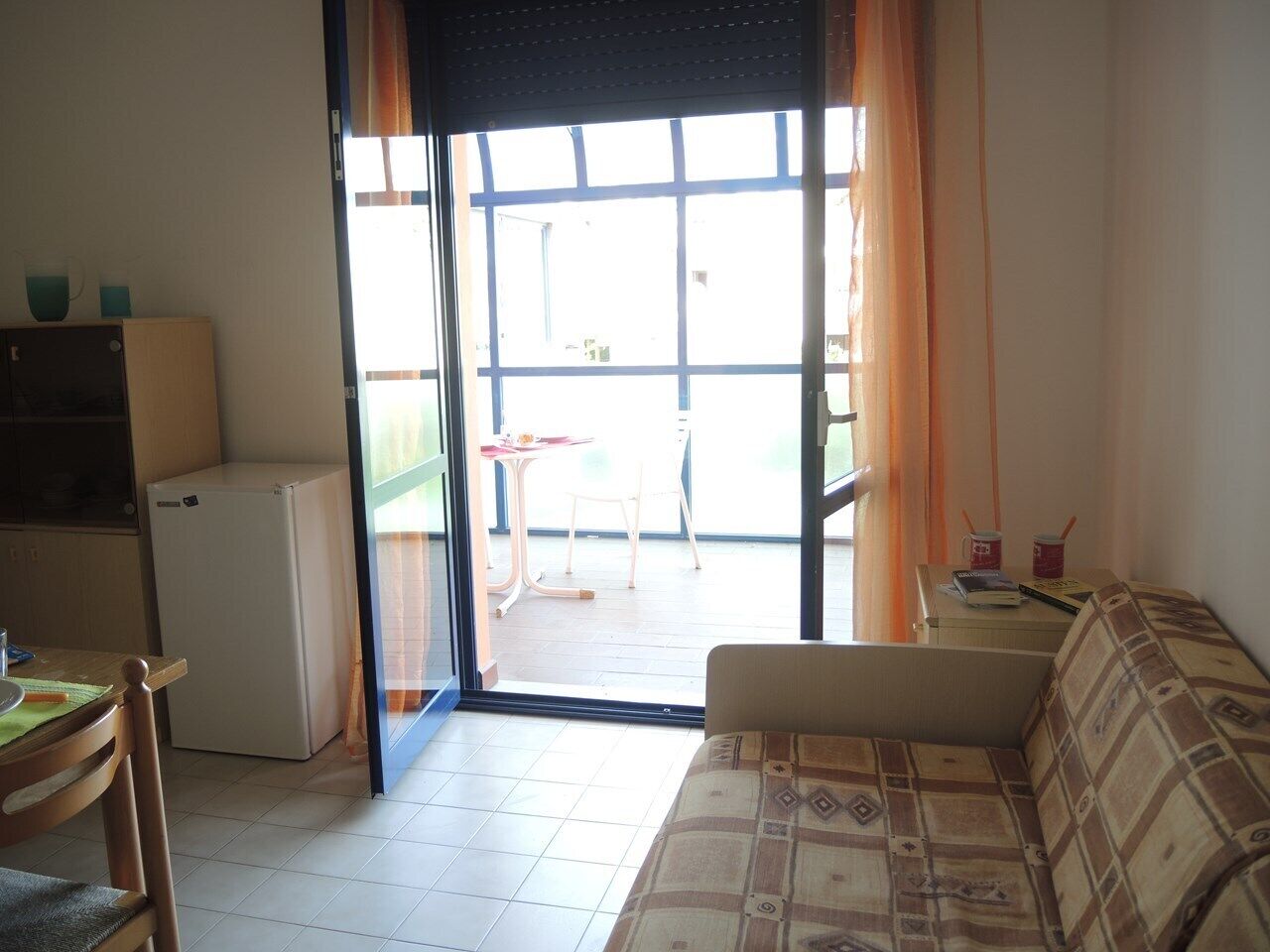 A compact living space with a kitchenette, a sofa, and a sliding glass door leading to an outdoor area with a table and chairs.
