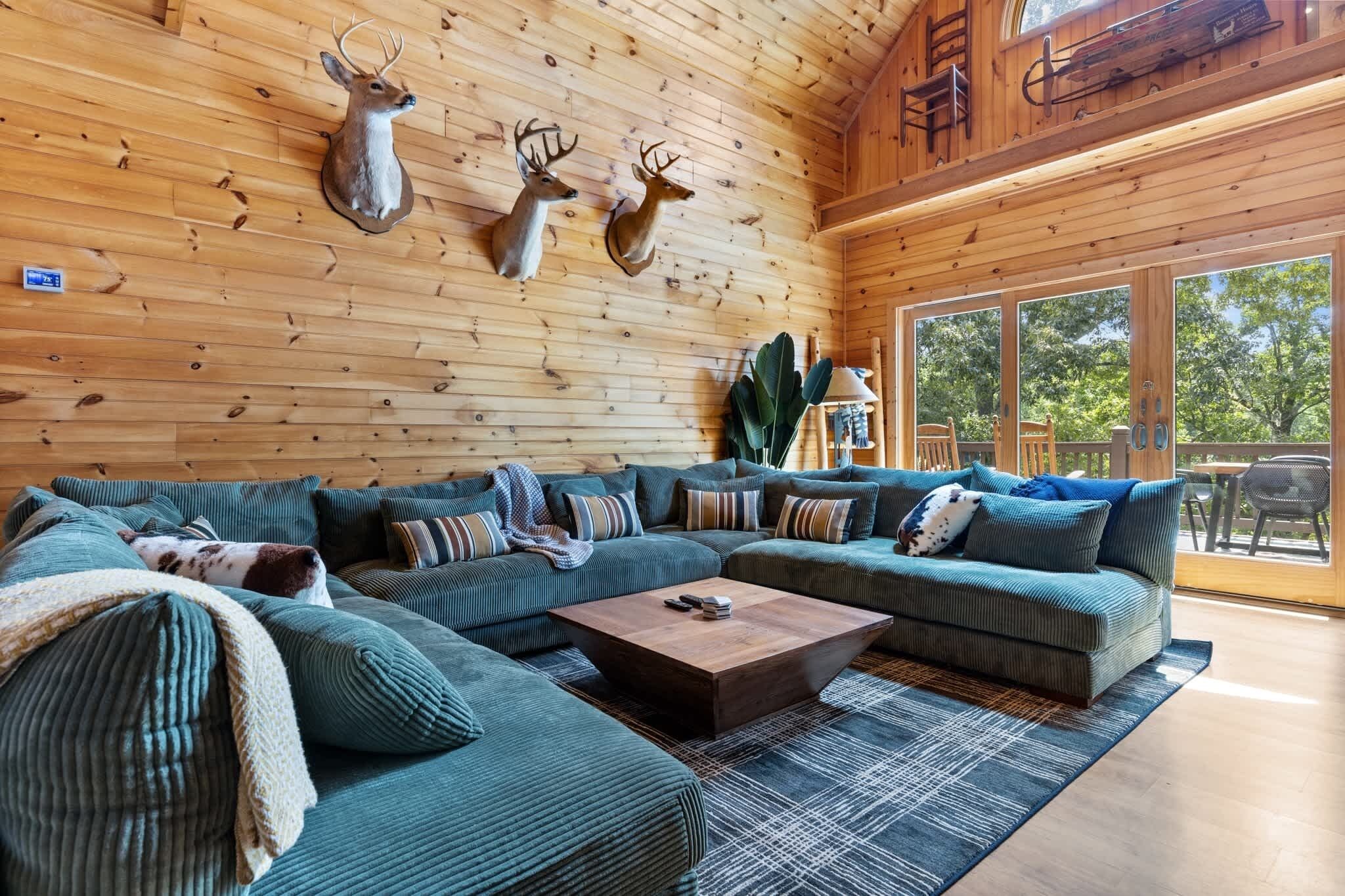 A wooden interior with a sectional sofa, mounted deer heads, and a large window.
