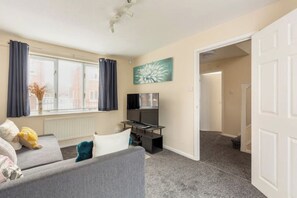 Relax in a comfortable seating area with a sofa and a small table, featuring a flat-screen TV and a window with curtains.