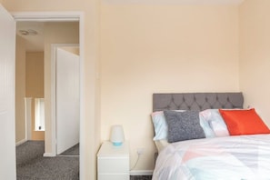 Cozy retreat with a tufted headboard and plush pillows, featuring a comfortable bed and convenient bedside table with a lamp.