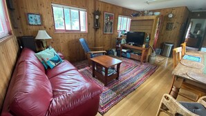 Ein gemütliches Wohnzimmer mit einer roten Ledersofa, Holzwänden, einem Fernseher und einem Essbereich mit Korbstühlen.