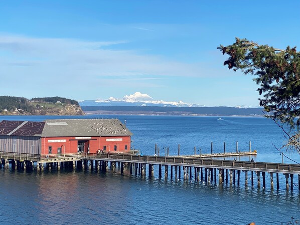 A red building with a sign reading "Gifts Food Coffee" on a pier extending into a body of water, with a mountain range in the background.