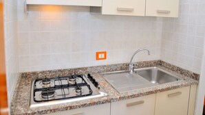 Een keuken met witte kasten, een granieten aanrecht, een roestvrijstalen spoelbak en een gasfornuis.