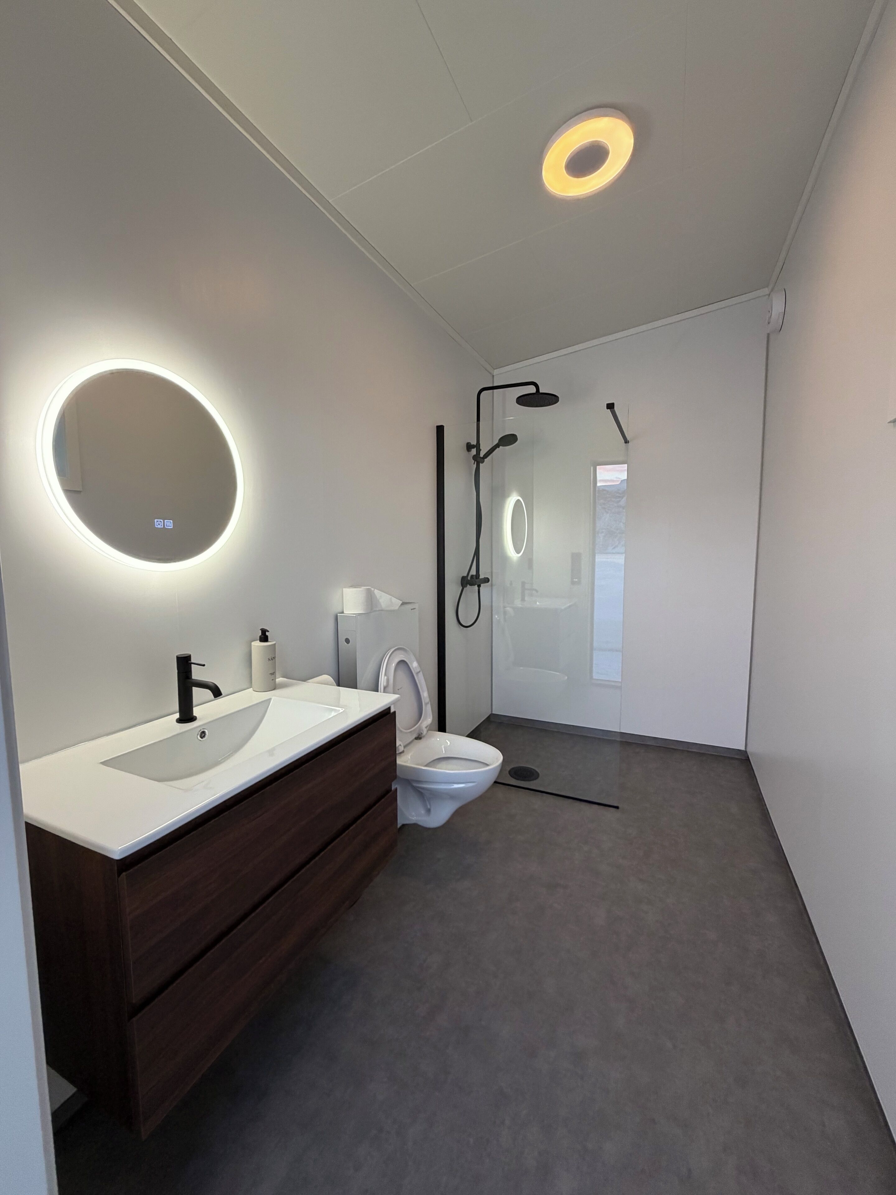 A modern bathroom with a white sink, dark wooden vanity, a toilet, and a glass-enclosed shower area.