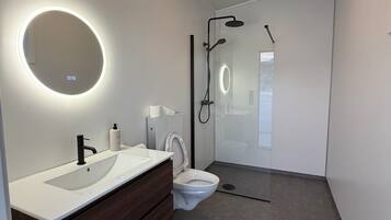 A modern bathroom with a white sink, dark wooden vanity, a toilet, and a glass-enclosed shower area.