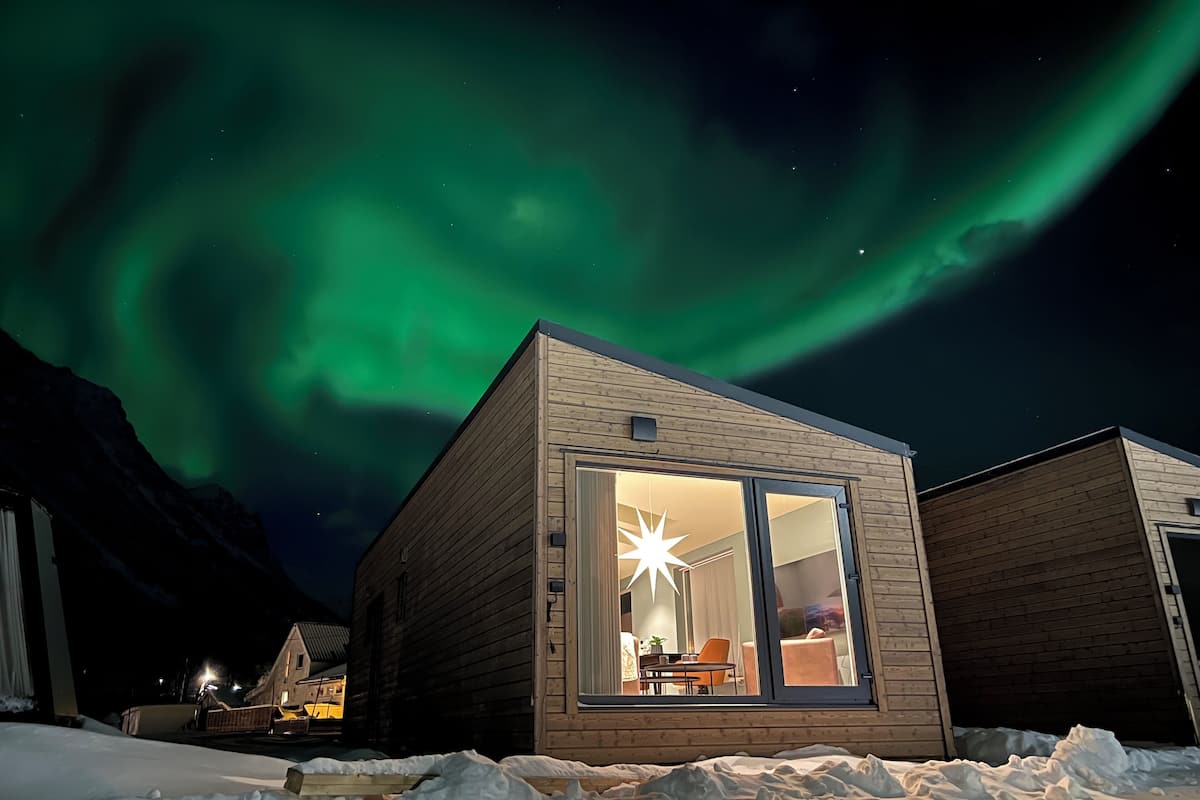 Una cabaña de madera con un amplio ventanal, una lámpara en forma de estrella y vistas de las auroras boreales.