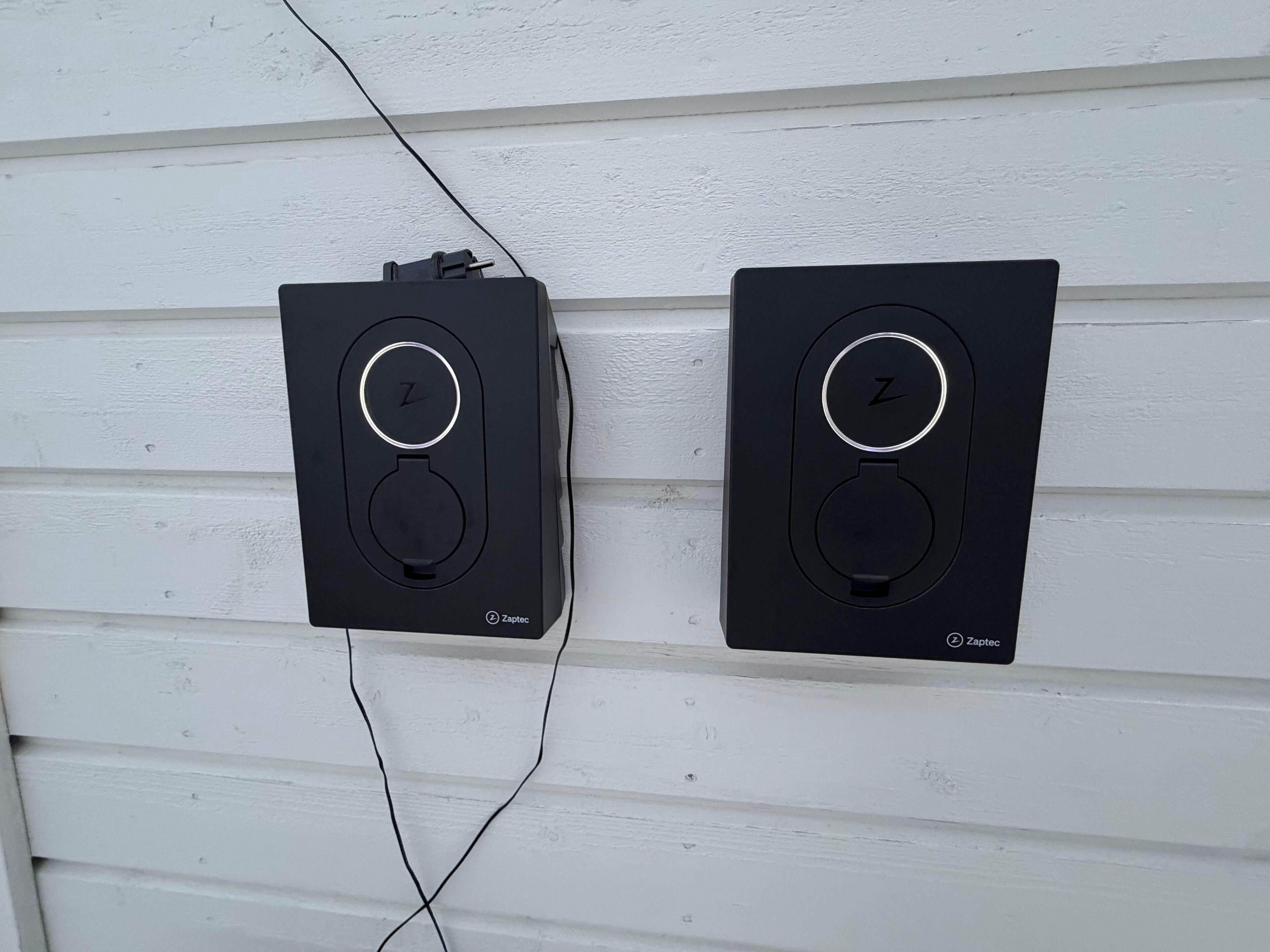 Dos altavoces negros fijados a la pared, con el nombre de la marca 'Zaptec' a la vista, conectados por un solo cable.