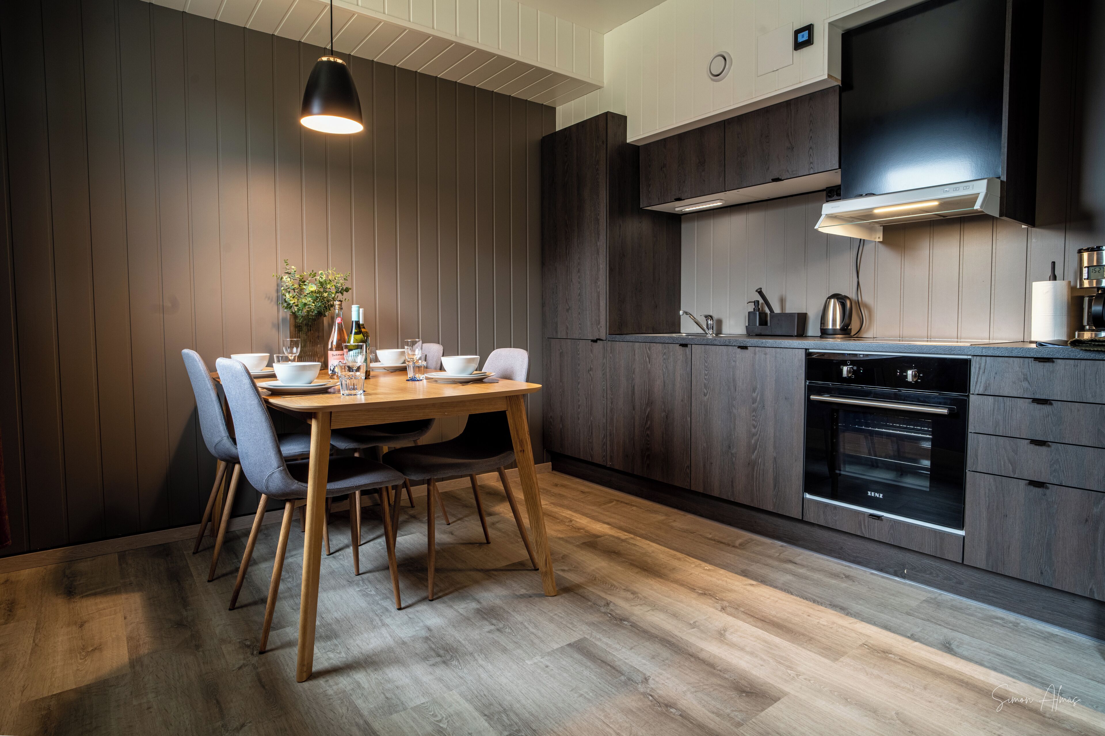 Una cucina moderna con mobili in legno scuro, forno integrato e zona pranzo con tavolo e sedie in legno.