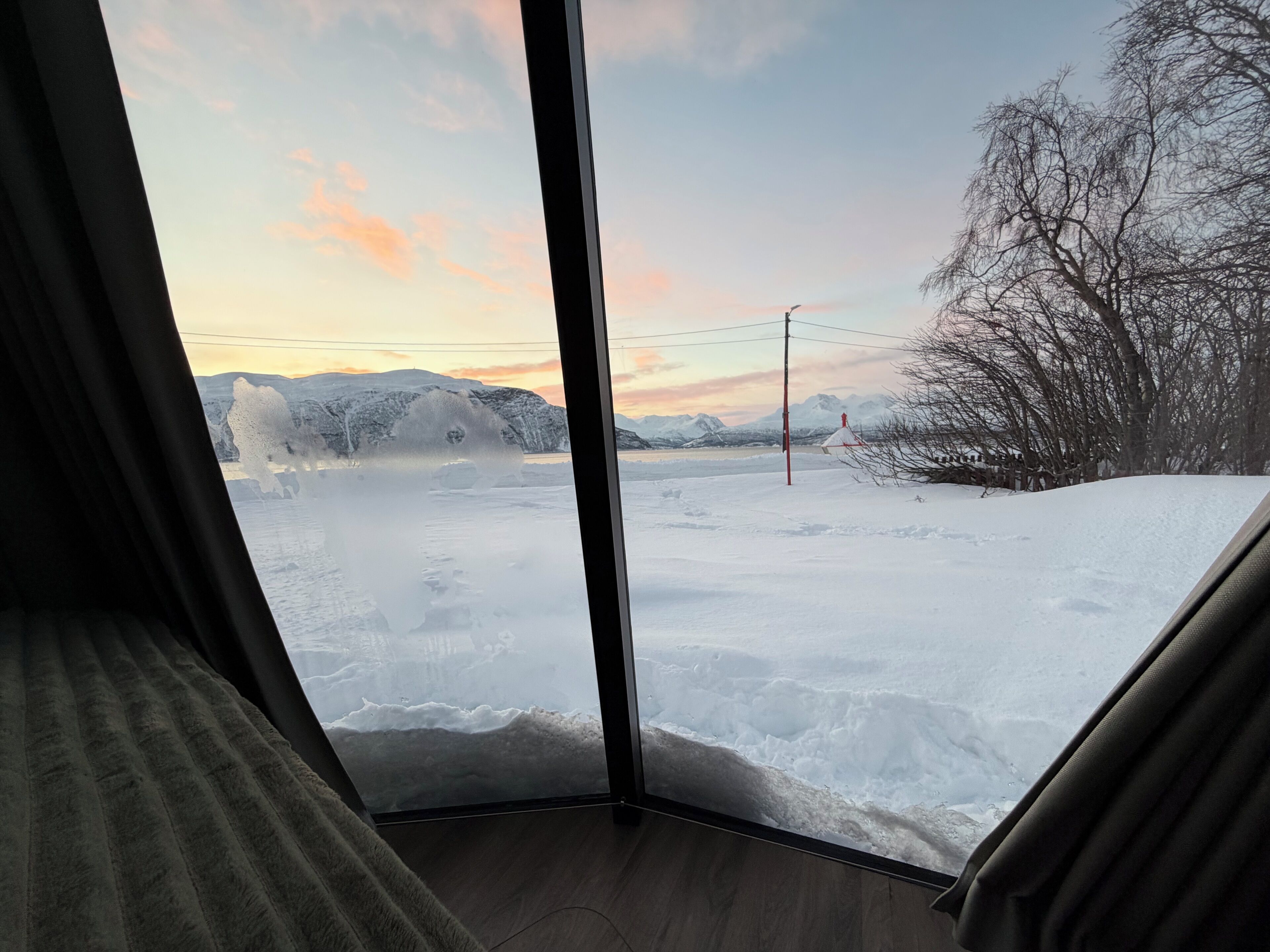 Ein Zimmer mit großem Fenster mit Blick auf eine verschneite Landschaft, Berge und einen klaren Himmel.
