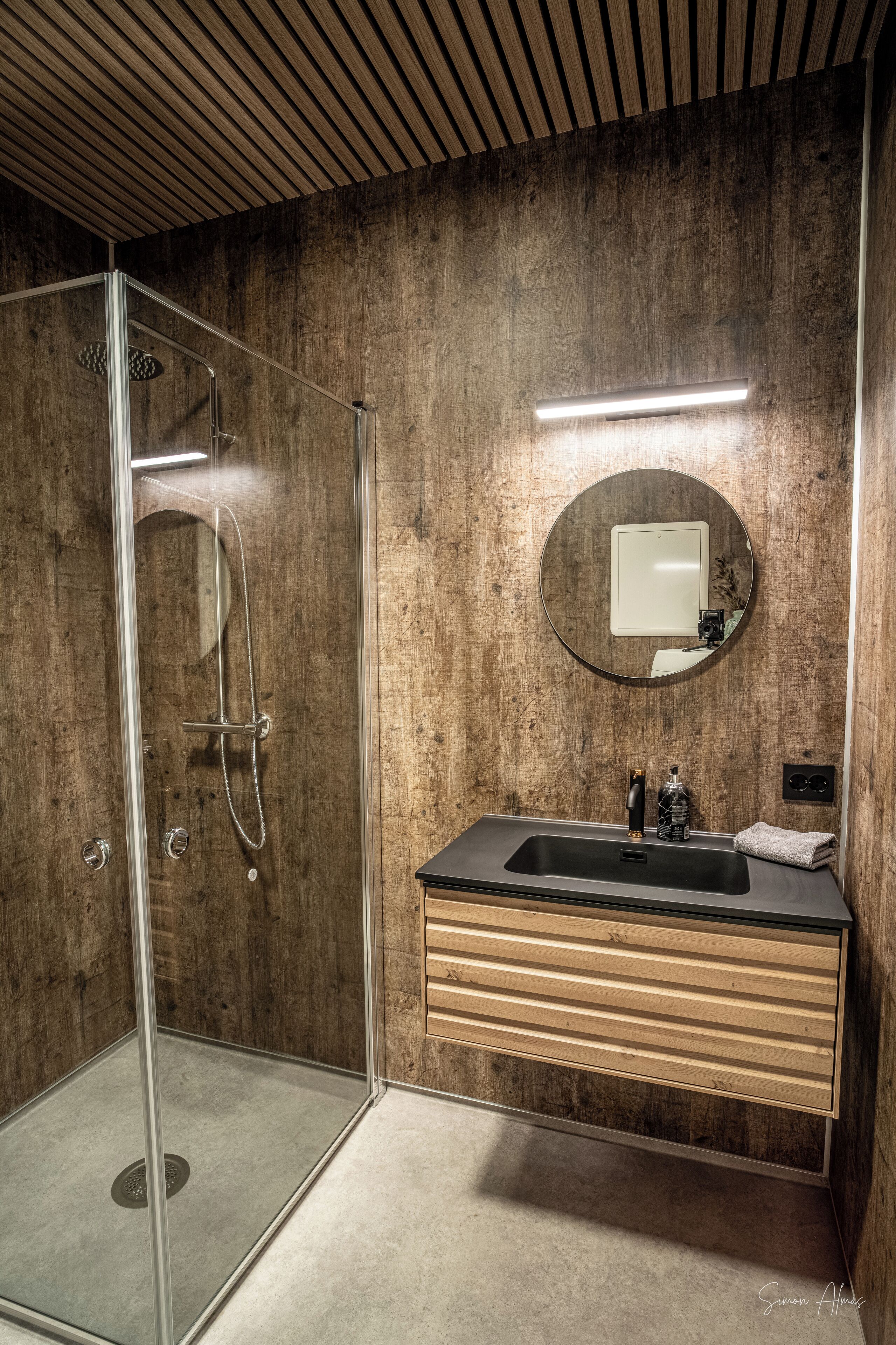 Un bagno moderno con doccia in vetro, mobile lavabo in legno e specchio tondo.